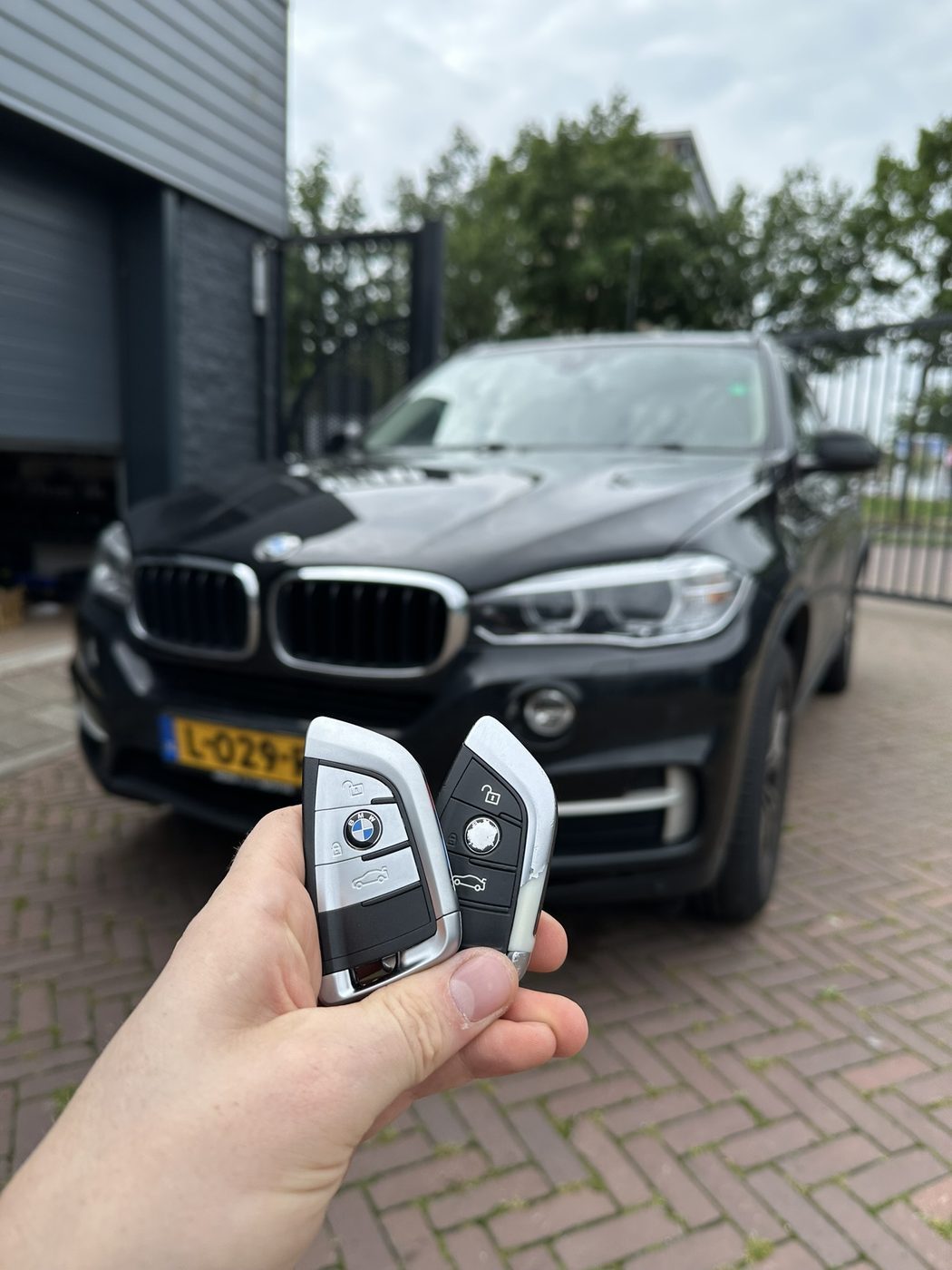 Twee BMW-smartkeys in de hand, met een zwarte BMW X5 op de achtergrond