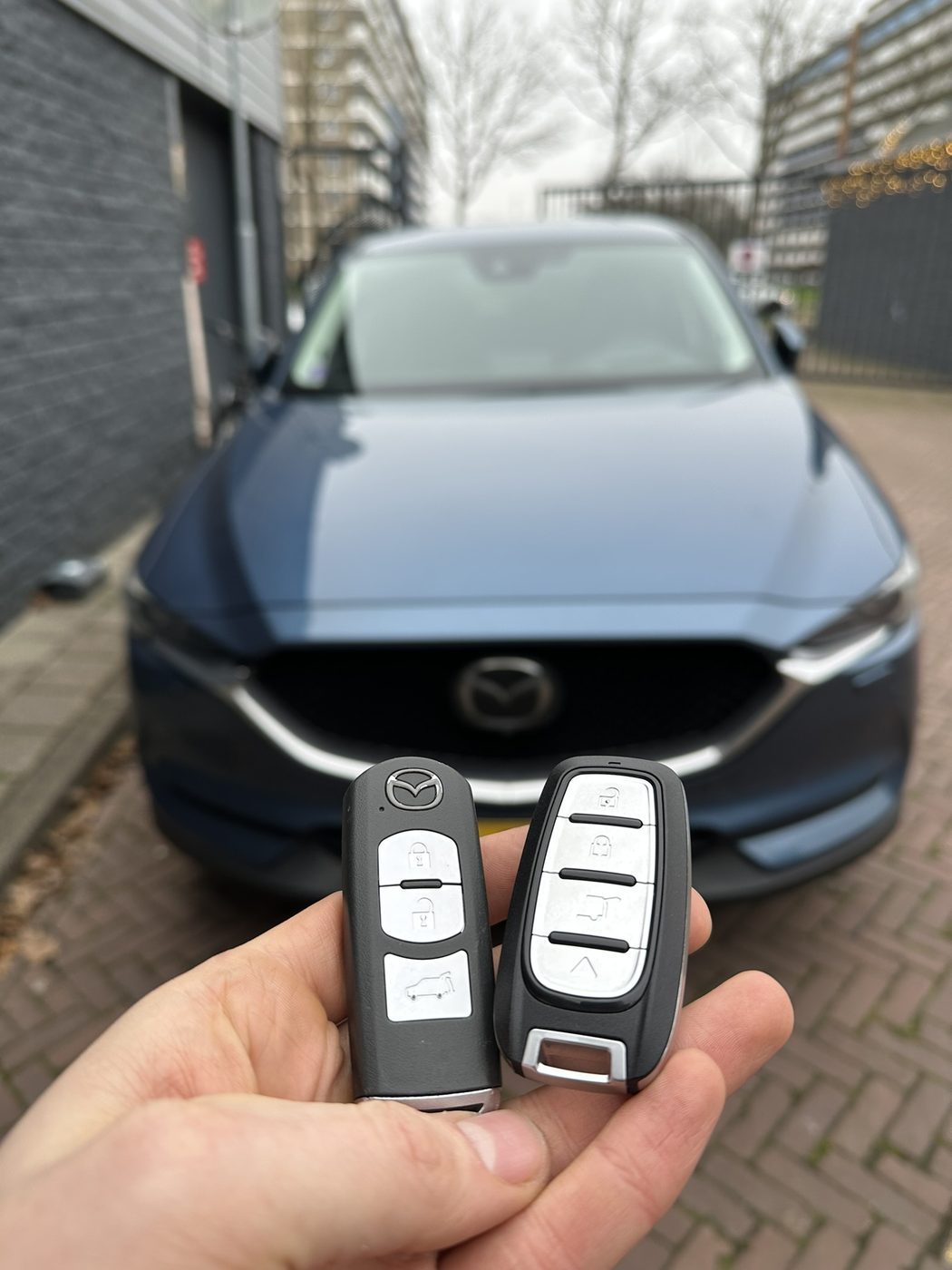 Twee Mazda-smartkeys in de hand, met de blauwe Mazda CX-5 op de achtergrond